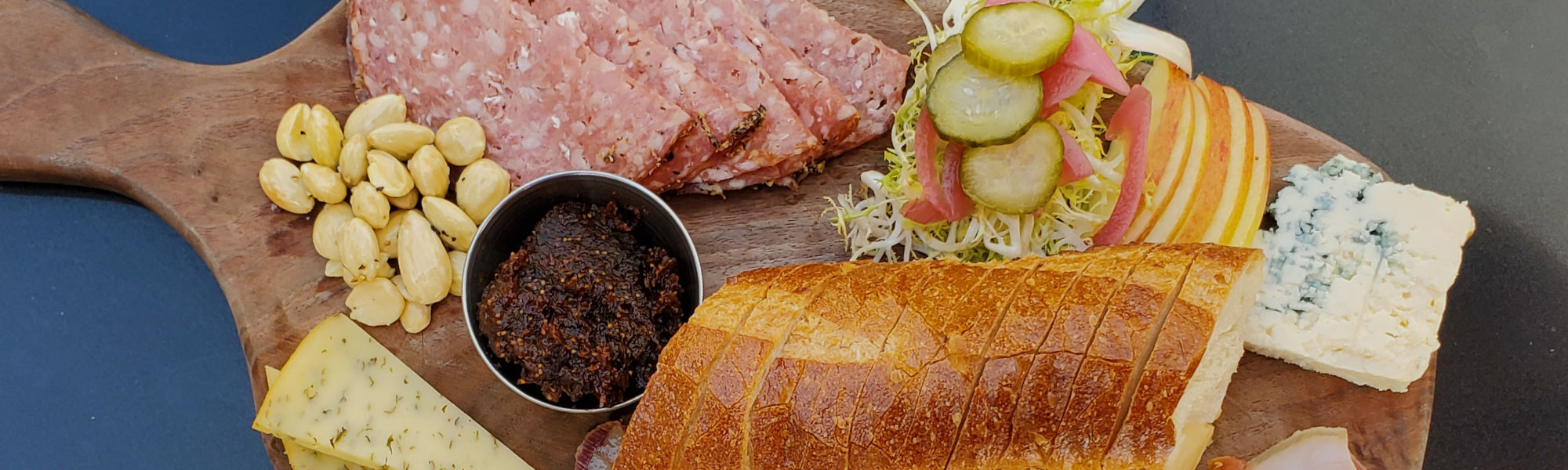 A charcuterie board with salami, almonds, fig jam, blue cheese and sliced baguette